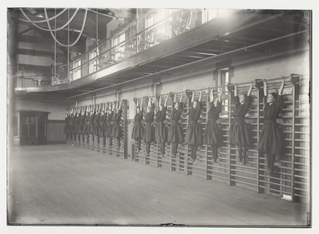 Historical photograph of girls stretching on wall bars