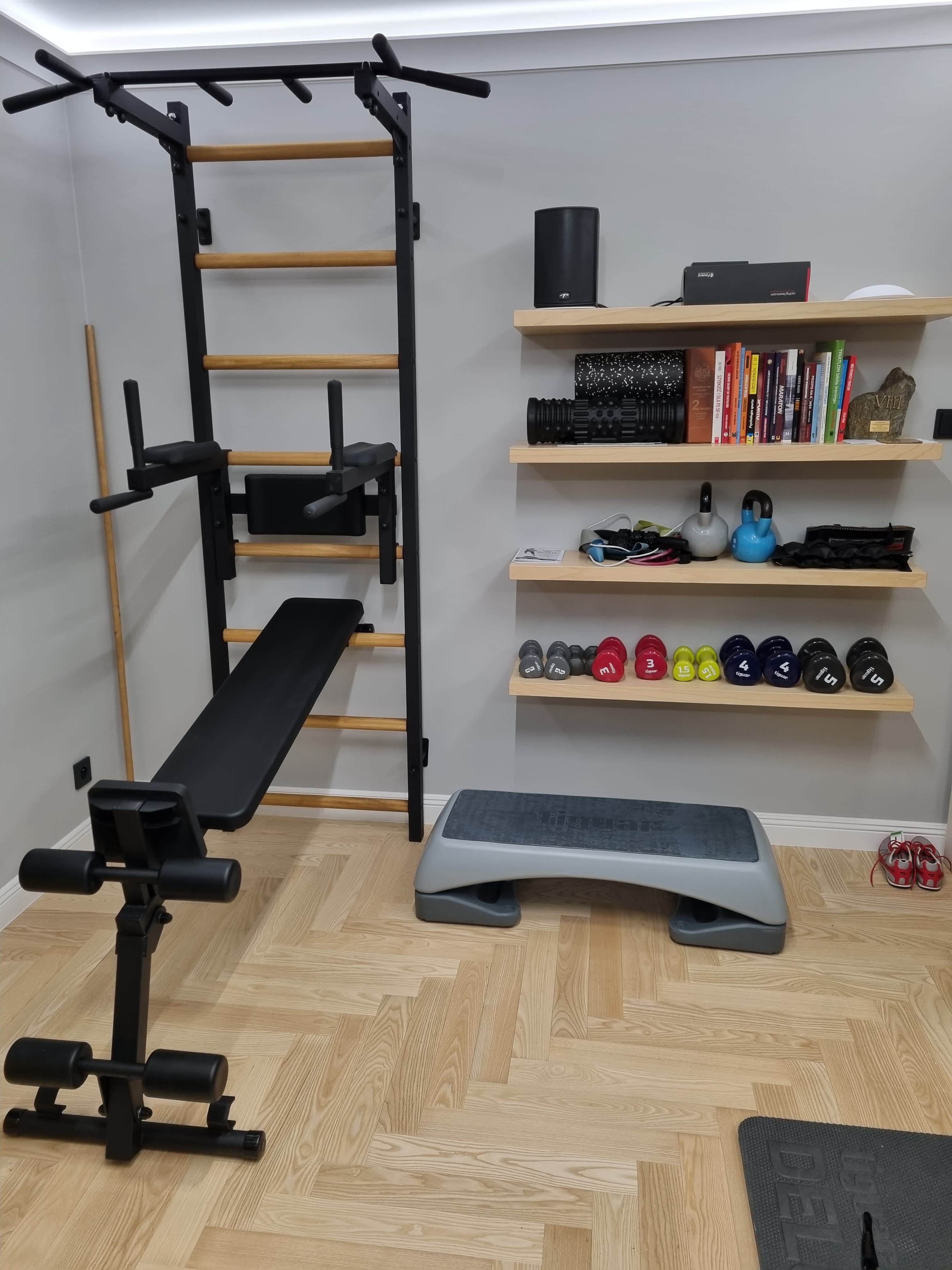 BenchK wall bars with a dip bar and bench attached, alongside dumbbells and mobility tools in a home gym