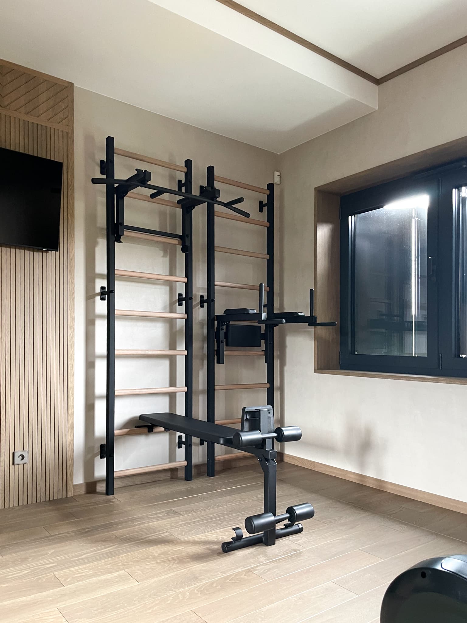 BenchK modular wall bar station with pull-up bar, dip attachment, and bench all mounted to the same bars in a home gym